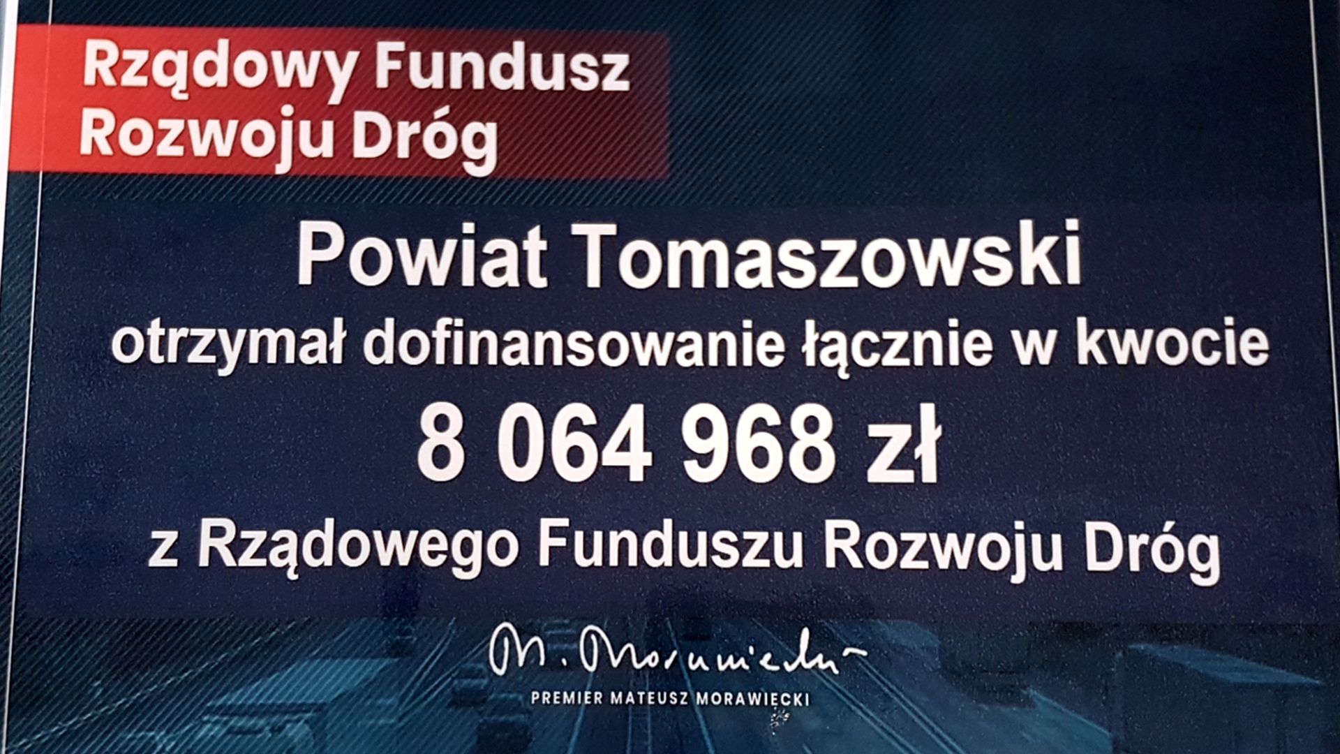 Na zdjęciu: tablica informacyjna, dotycząca pozyskanych środków finansowych dla Powiatu Tomaszowskiego w kwocie 8 064 968 złotych z rządowego Funduszu Rozwoju Dróg