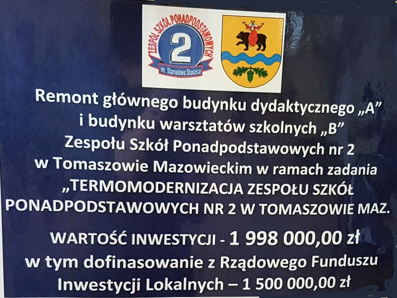 Na zdjęciu: baner z napisem Remont głównego budynku dydaktycznego „A” i budynku warsztatów szkolnych „B” Zespołu Szkół Ponadpodstawowych nr 2 w Tomaszowie Mazowieckim  w ramach zadania pn.: „Termomodernizacja Zespołu Szkół Ponadpodstawowych nr 2 w Tomaszowie Mazowieckim”. Waertość inwestycji – 1 998 000 zł. w tym dofinansowanie z Rządowego Funduszu Inwestycji Lokalnych – 1 500 000 zł. 